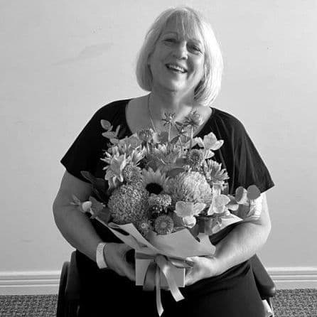 A lady sitting in a wheelchair with a warm smile and a large bunch of flowers on her lap.